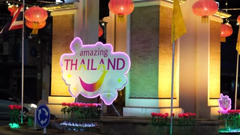 Erstaunliche-Thailand-Werbung-Vor-Einem-Beleuchteten-Gebäude-Mit-Menschen-Und-Motorrädern-Auf-Der-Straße
