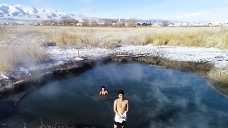 two-swimmers-male-and-female-standing-in-the-steam-of-saratoga-hot-springs-in-provo-utah-with-snow-all-over-the-ground-mid-day