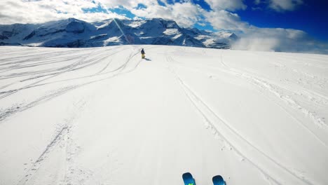 Skiing-in-powder-with-a-person-skiing-in-front-with-mountains-as-a-backdrop