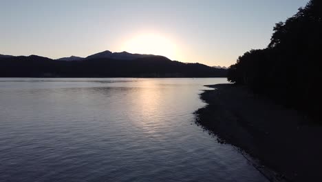 Cinematic-establishing-shot-moving-backwards-from-the-lake-Nahuel-Huapi-at-sunset-in-Villa-La-Angostura,-Patagonia-Argentina