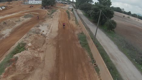 Wide-aerial-FPV-slow-motion-follow-of-motocross-rider-jumping-high,-sky-reflect-in-mud