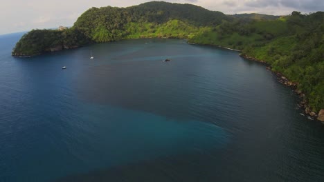 Drone-fly-over-a-tropical-bay-with-lush-jungle-and-a-few-boats-moored-up