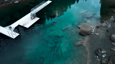 Aerial-view-of-a-man-in-a-neopren-swimming-on-a-board-in-a-pristine-blue-water-lake-Caumasee-in-Switzerland