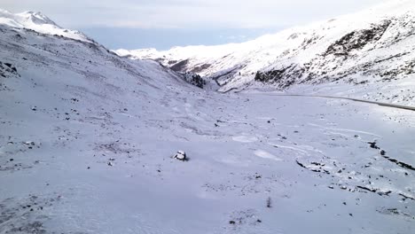 Rückansicht-Eines-Mannes-In-Einer-Roten-Jacke-Aus-Der-Luft,-Der-An-Einem-Wintertag-Am-Fluela-Pass-In-Der-Schweiz-Auf-Einen-Schneebedeckten-Bergpass-Blickt