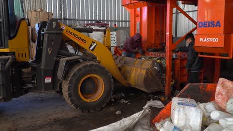 Two-workers-load-a-bulldozer-with-compacted-garbage-inside-a-waste-processing-plant
