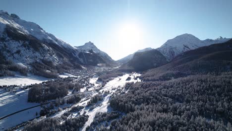 Aerial-view-of-snow-covered-mountain-landscape-with-forests-and-villages-on-a-sunny-day-in-Pontresina,-Switzerland