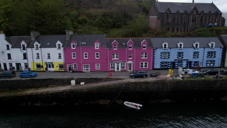 Aerial-view-passing-charming-Portree-Harbour-colourful-Scottish-coastal-vacation-houses-on-dusk-waterfront