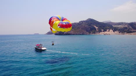 Parasailing,-Tourists-On-Parachute-Towed-Behind-The-Speedboat-In-Tsambika-Beach,-Greece