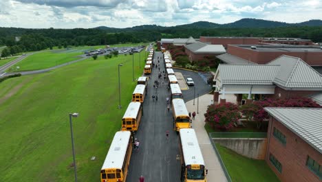 Students-outside-exterior-of-school-building-get-on-yellow-school-bus-in-USA