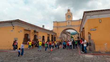 Static-shot-of-people-walking-on-street-under-Santa-Catalina-Arch-in-Antigua,-Guatemala-at-daytime