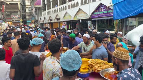 High-angle-shot-over-locals-bargaining-before-purchase-in-an-old-busy-traditional-street-Iftar-food-market-in-Dhaka,-Bangladesh-surrounded-by-houses-on-all-sides