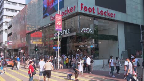 Chinese-pedestrians-and-shoppers-rush-and-walk-at-a-hectic-and-busy-zebra-crossing-junction-in-front-of-the-American-multinational-sportswear-and-footwear-retailer,-Foot-Locker,-store-in-Hong-Kong