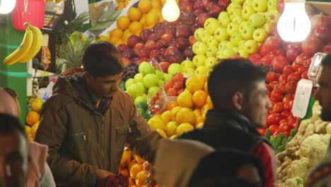 Young-merchant-organising-fruit-on-market-stall-and-greeting-customers-in-Tajrish-Bazaar-in-Tehran,-Iran