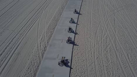 Aerial-Drone-Shot-of-5-People-on-Bikes-Riding-on-Beach-Boardwalk