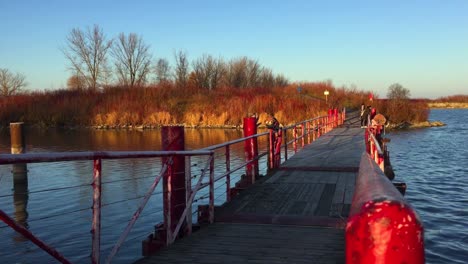Wide-shot-of-late-autumn-sunlight-on-a-vibrant-red-floating-bridge-as-hikers-walk-in-Tommy-Thompson-Park