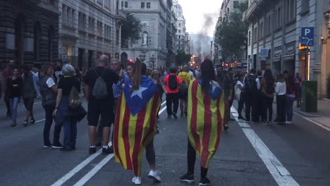Zwei-Mädchen-Tragen-Die-Estelada-Flagge-Auf-Der-Via-Laietana-Während-Des-Katalanischen-Protests-Mit-Einem-Großen-Feuer-Und-Schwarzem-Rauch-Im-Hintergrund