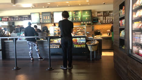 Customers-waiting-in-line-at-a-Starbucks,-cleaning-lady-walking-by
