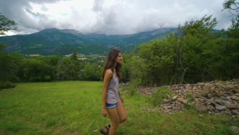 A-brunette-woman-on-a-hike-walking-through-a-lush-green-meadow-in-a-clearing-within-the-forest-on-a-cloudy-day