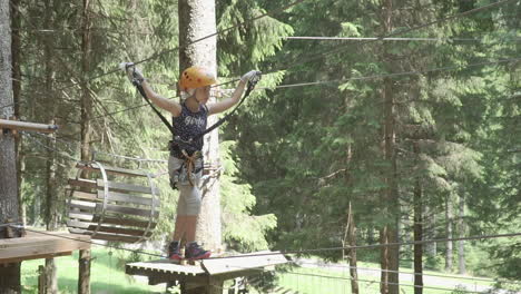 Little-girl-with-red-hair-walks-on-a-rope-in-adventure-park-in-the-Italian-Alps,-slow-motion