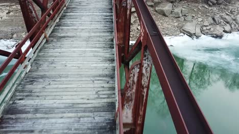 Close-up-of-Rusty-Old-Red-Footbridge-Over-Icy-River