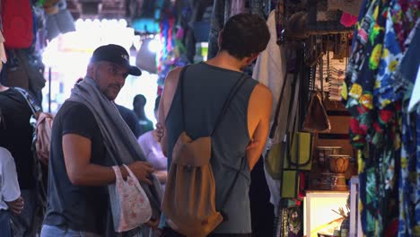 Turistas-Masculinos-Probándose-Ropa-En-El-Mercado