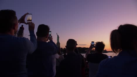 silhouette-shot-of-tourists-taking-pictures-of-statue-of-liberty-from-a-boat-at-dusk