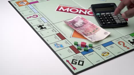A-Black-male-Accountant-counting-fifty-pound-notes-on-a-Monopoly-board-with-a-calculator