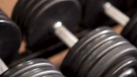 Extreme-closeup,-slow-slider-shot-to-the-left-looking-down-on-row-of-dumbbells-on-a-rack
