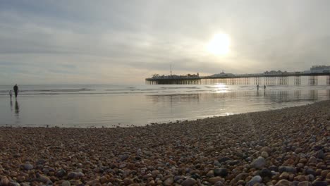 Brighton-Beach-Mit-Sonnenuntergang-über-Dem-Pier-Und-Menschen,-Die-Durch-Die-Wellen-Gehen