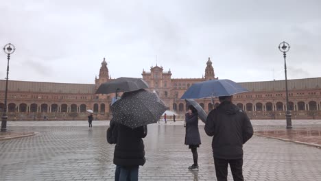 Moving-toward-tourists-with-umbrellas-in-rainy-Plaza-de-Espana,-Seville,-SLOWMO