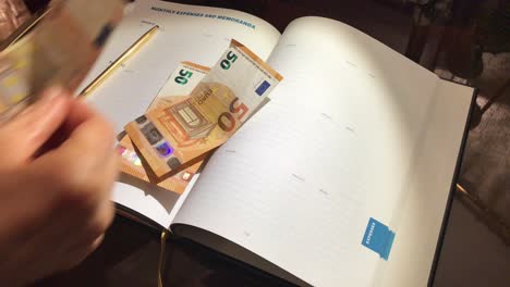 Woman-hand-counting-fifty-euro-bills-on-open-business-planner