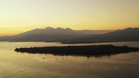 Nebliger-Gelber-Himmel-Nach-Sonnenuntergang-über-Dem-Horizont-Der-Berge,-Der-Das-Sonnenlicht-Auf-Der-Ruhigen-Meeresoberfläche-Um-Die-Silhouette-Der-Tropischen-Insel-Bali-Reflektiert