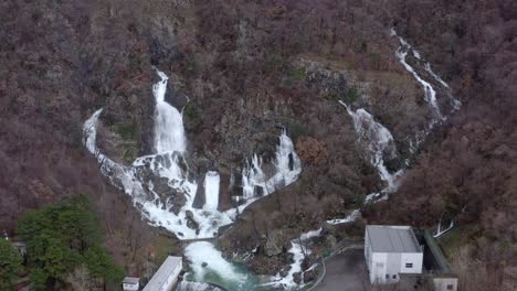 Aerial---Multiple-waterfalls-coming-out-of-rocky-hillside-joining-streams,-fly-in