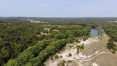 Pan-left-showing-hill-country-with-fields,-trees,-and-small-portion-of-the-river---Aerial-footage-of-the-Blanco-river-in-Wimberly,-TX