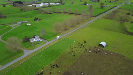 Aerial-drone-shot-of-RV-driving-down-a-country-road-with-green-paddocks-in-New-Zealand