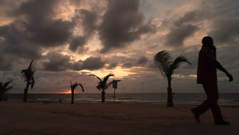 African-sillouette-man-on-mobile-phone-walks-past-on-Senegambia-Beach-Serrekunda-The-Gambia-at-sunset