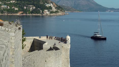 The-southern-section-of-the-wall-in-old-town-Dubrovnik-with-very-few-tourists-due-to-covid-and-a-sailboat-drifting-by