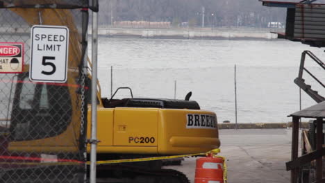 Breeze-Yellow-Crane-Works-on-Construction-Site-on-East-River-Waterfront-in-Brooklyn,-Close-Up,-Bikers-Ride-By-Watching