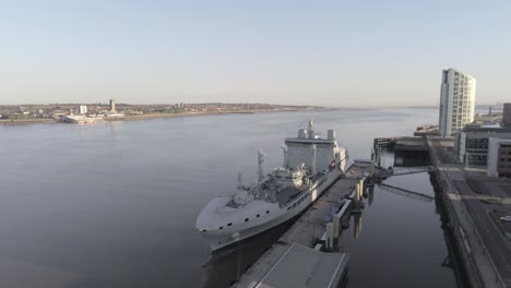 Liverpool-waterfront-aerial-view-royal-navy-military-ship-sunrise-high-rise-buildings-skyline-slow-descend