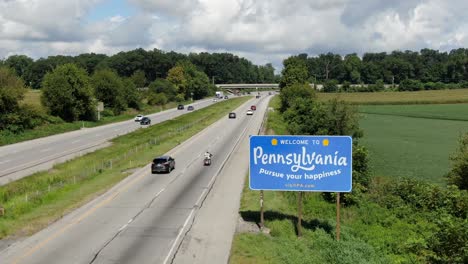 Welcome-to-Pennsylvania-sign-along-highway,-arriving-on-road-from-Delaware,-Maryland,-New-York,-Ohio,-New-Jersey,-West-Virginia