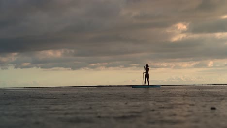 Silhouette-of-girl-on-stand-up-paddle-moving-on-ocean-during-sunset-and-rain
