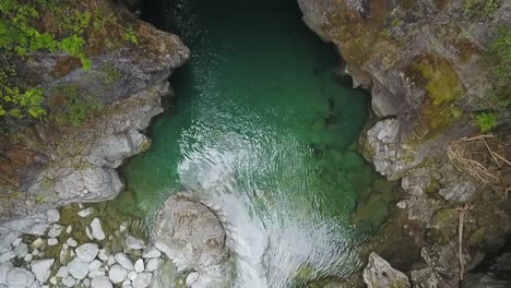 Aerial-tilt-up-of-Rio-Azul-stream-running-between-rocky-cliffs-surrounded-by-vegetation,-El-Bolsón,-Patagonia-Argentina