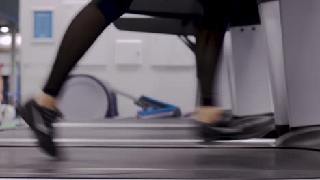 One-person-running-on-a-treadmill-in-black-leggings-and-trainers,-close-up
