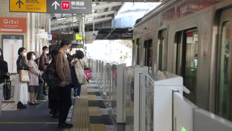 Zug-Nähert-Sich-Einem-Bahnsteig-Mit-Pendlern,-Die-Aufgrund-Einer-Pandemie-In-Tokio,-Japan,-Gesichtsmasken-Tragen