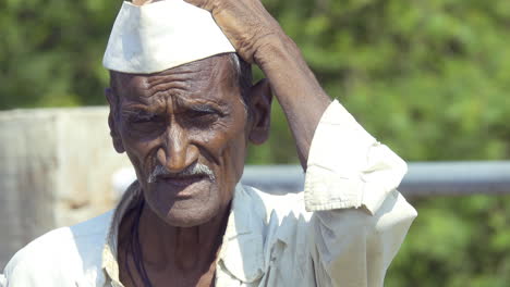 An-old-poor-farmer-from-Indian-rural-village-area-of-Latur-is-seen-scratching-his-head-and-avoiding-the-heat-of-the-sun-by-looking-away
