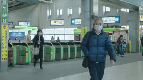 Personas-Con-Máscaras-Caminando-Por-Las-Puertas-De-Entrada-En-La-Estación-Shinagawa-Jr-En-Tokio---Plano-General,-Cámara-Lenta