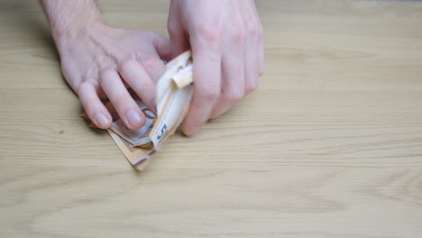 Male-hands-piling-and-shuffling-50-euro-paper-money-bills-on-a-wooden-table