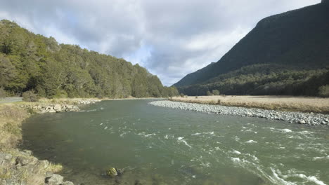 Running-river-surrounded-by-lush-forrest-and-mountains-in-New-Zealand's-South-Island