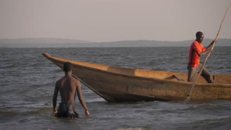 Slow-motion-shot-of-an-African-fishermen-pushing-his-traditional-wooden-canoe-passed-swimmers-on-Lake-Victoria