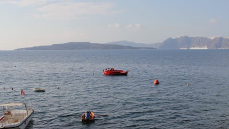 A-man-is-paddling-in-the-aegean-sea,-inside-the-Santorini-caldera